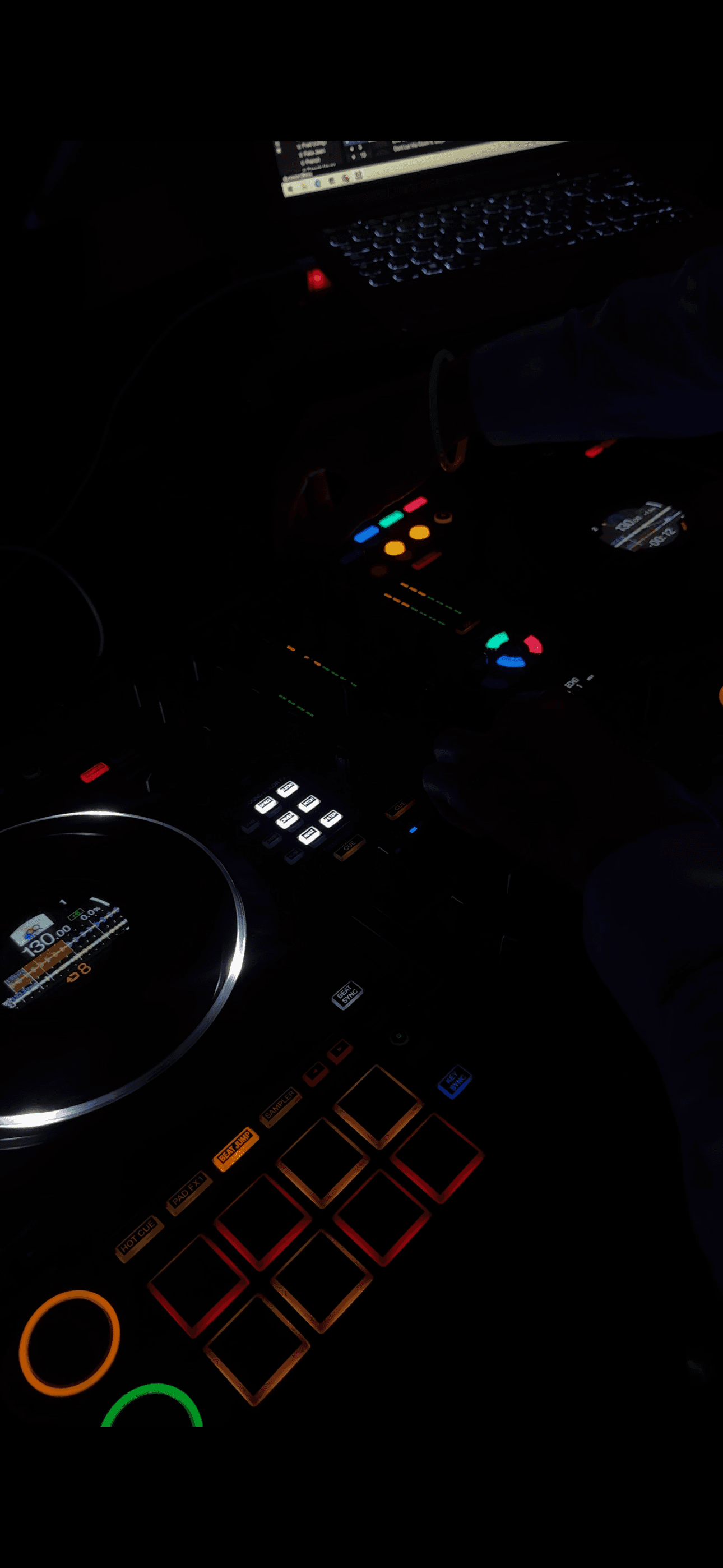 Nahaufnahme eines DJ-Controllers mit bunten, leuchtenden Tasten und Jogwheel in einer dunklen Umgebung.